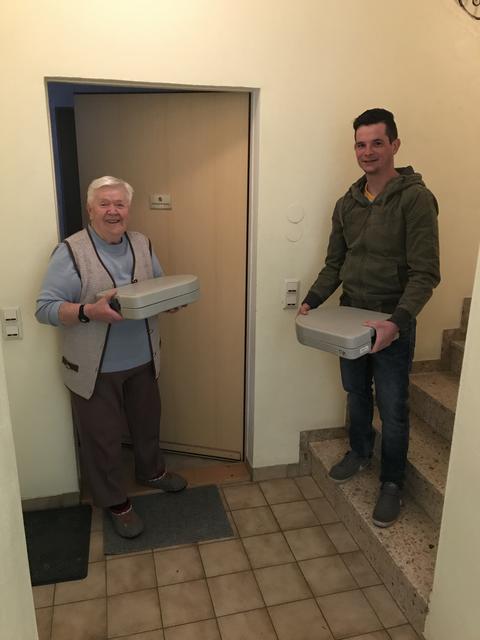 Die mit warmen Essen beladene Box wird vom Essenfahrer auf die Stufe gestellt und nach dem Klingel an der Wohnungstür von der Bezieherin abgeholt. Die leere Box nimmt der Essenfahrer mit. Essenbezieherin seit zehn Jahren Elisabeth Trausnitz (li.), der Muhrer Gemeindejugend-Obmann Thomas Aigner (re.).