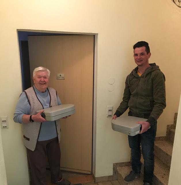 Die mit warmen Essen beladene Box wird vom Essenfahrer auf die Stufe gestellt und nach dem Klingel an der Wohnungstür von der Bezieherin abgeholt. Die leere Box nimmt der Essenfahrer mit. Essenbezieherin seit zehn Jahren Elisabeth Trausnitz (li.), der Muhrer Gemeindejugend-Obmann Thomas Aigner (re.).