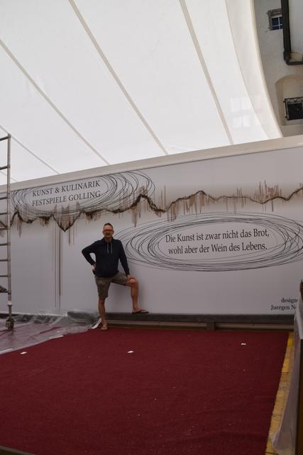 "Die Kunst ist zwar nicht das Brot, wohl aber der Wein des Lebens." Der Künstler Jürgen N. Fux vor dem von ihm entworfenen Bühnenbild der Kunst und Kulinarikfestspiele der Burg Golling.