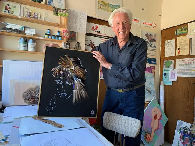 Im Atelier: Kurt Scharfegger mit seinem neuesten Werk – eine Collage. Sie zeigt ein weibliches Gesicht mit Vogelfedern als Frisur.