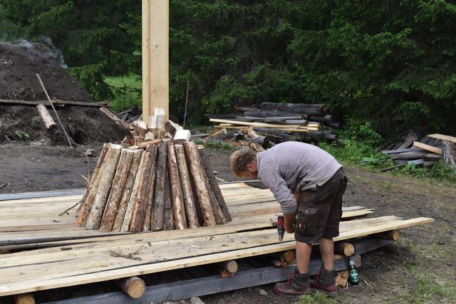 Andreas Zehner befestigt den Holzboden für den zweiten Rundholzmeiler. Im Hintergrund der erste Meiler in der Endphase.
