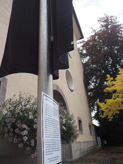 Eine schwarze Fahne und darunter ein Schild mit der Eklärung vor der Pfarrkirche in Reutte.