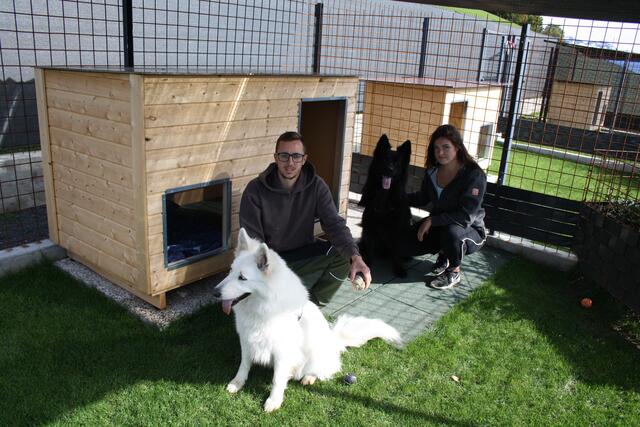 Luna und Michael Pließnig mit den Hunden Diago und Akita vor einer großen Hundehütte.