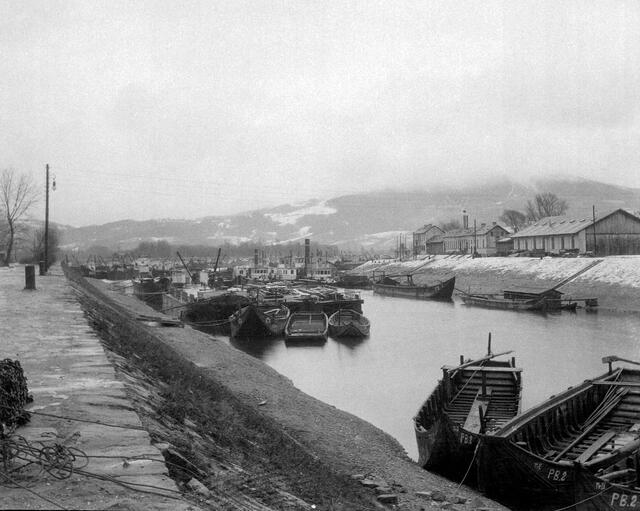 Damals 1916: Holzboote im Winterhafen
Zwischen 1897 und 1900 wurde der rund einen Kilometer lange Linzer Winterhafen angelegt. Er endete bei der einstigen Ausmündung des Fabriksarms in die Donau, welcher im Jahr 1892 zugeschüttet wurde. Die zur Zeit des Ersten Weltkriegs entstandene Winteraufnahme zeigt neben den Dampfschiffen im Hintergrund noch einige Lastkähne aus Holz, die zum Schutz vor den Eisstößen der Donau im Hafenbecken vertäut worden sind. | Foto: Archiv der Stadt Linz