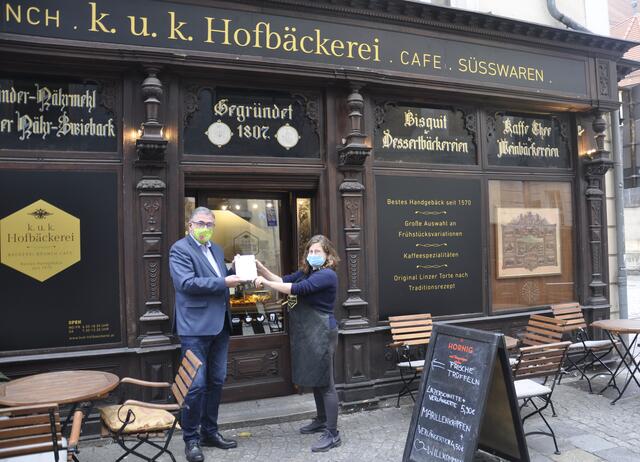 Tourismusdirektor Georg Steiner übergibt die Gästeregistrierungsformulare an Corinne Wandling von der KuK Hofbäckerei in Linz. | Foto: Linz Tourismus
