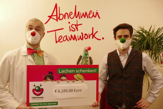 Mit dem Markenzeichen der CliniClowns auf der Nase und einem Lächeln hinter der Maske: Siegfried Perchtold von easylife (re.) übergibt den symbolischen Scheck über 6.289 Euro an Clown Dr. Hänsel, von den CliniClowns.