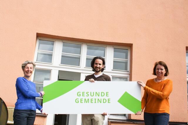 Präsentieren das neue Ortsschild der "Gesunden Gemeinde": AVOS-Gesundheitsreferentin Mag. (FH) Anna Hofer, AVOS-Gesundheitsreferent Mag. Mario Proske, BSc, und AVOS-Bereichsleiterin Mag. Patricia Lehner.