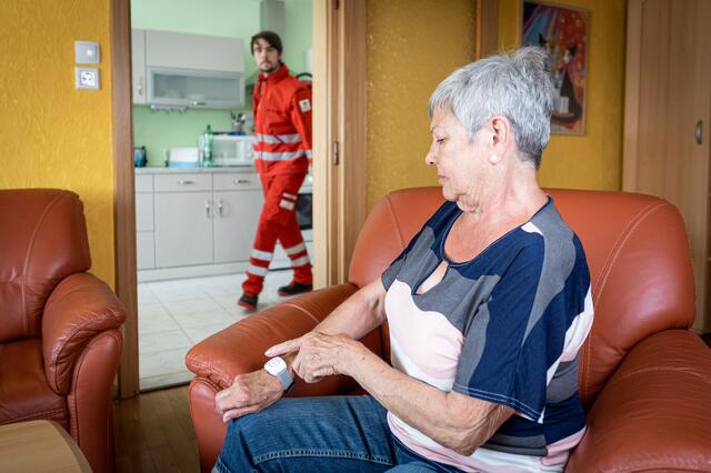 Rotkreuz-Sanitäter helfen einer Dame, nachdem sie auf ihrem Rufhilfe-Armband den Notrufknopf gedrückt hat.