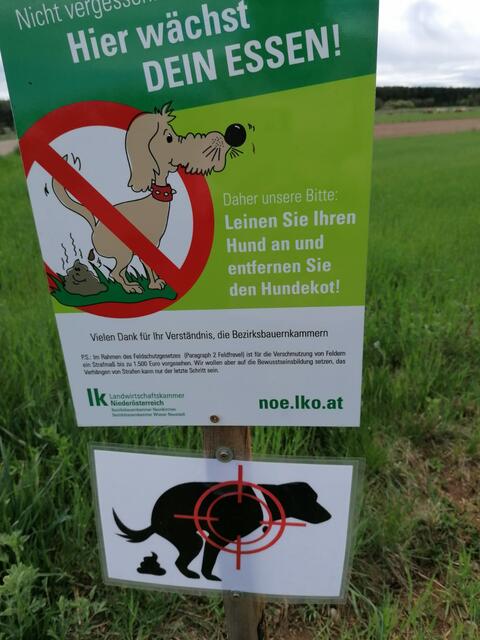 Die Zusatztafel suggeriert, dass Hunde, die in Felder kacken ins Fadenkreuz rücken.