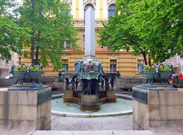 In einem niedrigen runden Becken findet sich ein dreipassförmiger Sockel, auf dem dreimal fünf Putten drei Wasserbecken, die durch drei Figurengruppen verbunden sind, tragen