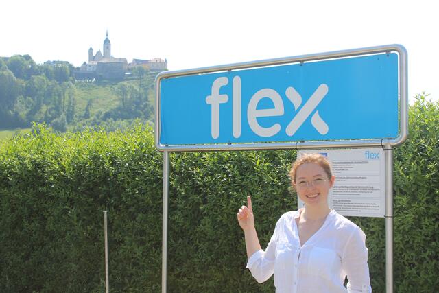 Die fröhliche Emilia vor dem Schild ihres Lehrbetriebes in Althofen.