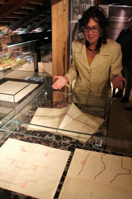 Kuratorin Sylvia Mader zeigt auf die Vitrinen: Querprofile (1901, 1908) und Lageplan Landeck (1918), Originale von Land Tirol/Abteilung Mobilitätsplanung. Im Hintergrund Modellzüge der Vinschgerbahn: Dampflok aus dem Jahre 1911; Triebwagen „Littorina“ aus den 1940er Jahren, Leihgabe von Eisenbahnwelt Rabland und 
 | Foto: Olaf Sailer
