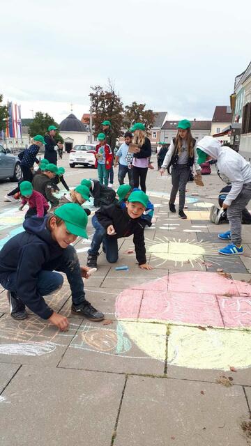 Die Kinder der Volksschule bemalten einen Straßenabschnitt auf dem Hauptplatz mit Natur- und Umweltmotiven.