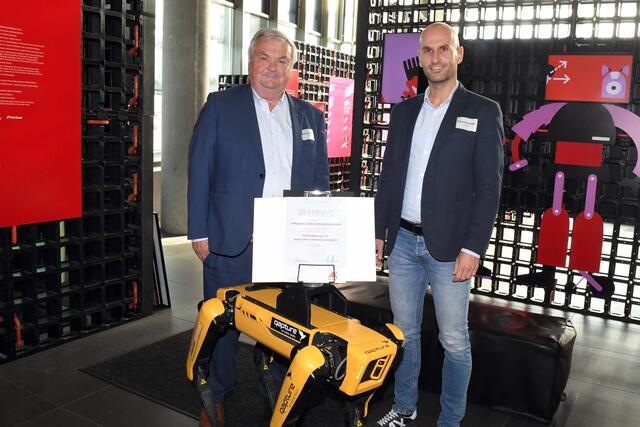 AK-Präsident Johann Kalliauer (links) übergibt mit Roboterhund Spot das Zertifikat an eMagnetix-Geschäftsführer Klaus Hochreiter.