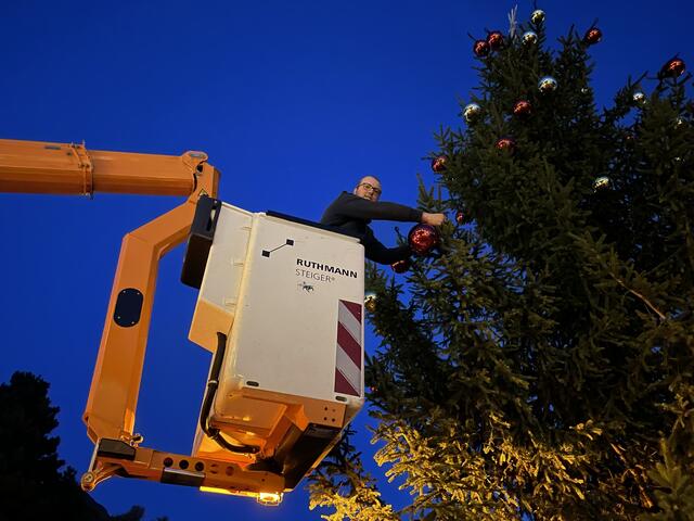 Gemeindemitarbeiter Philip Kröll befestigt den Christbaumschmuck an der Tanne. Schon bald wird der Baum vielen Menschen große Freude bereiten. | Foto: Kendlbacher