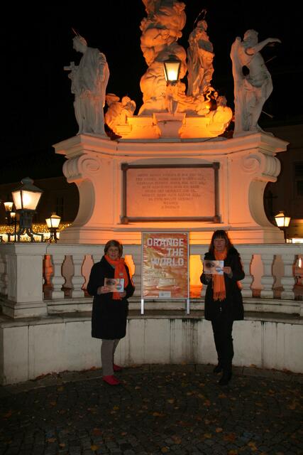 Lilli Frömmer-Scherabon, Präsidentin des Soroptimist Club Mödling, und Martina Zöchling-Feike setzen vor der orange beleuchteten Pestsäule in Mödling ein Zeichen gegen Gewalt an Frauen und Mädchen.