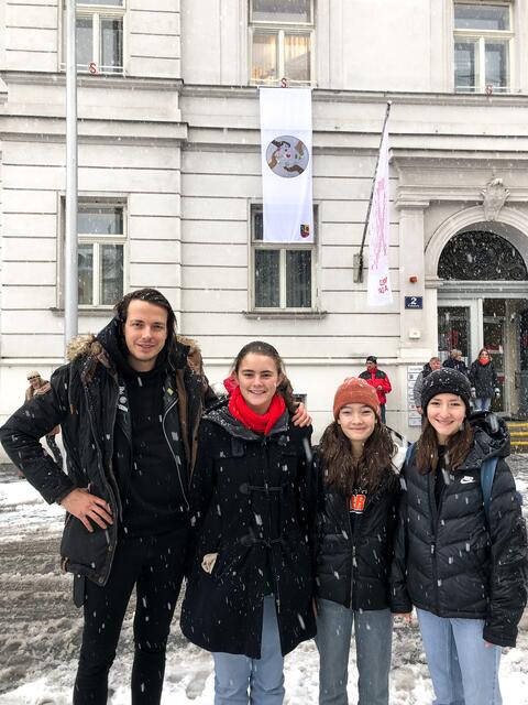Die drei Siegerinnen Elena Kinsky, Paula Kappel und Paula Unbehaun posieren stolz mit Bezirksrat Dominik Wlažny (Bierpartei) vor ihrer selbstgestalteten Menschenrechtsfahne am Amtshaus Simmering. | Foto: Pogo's Empire