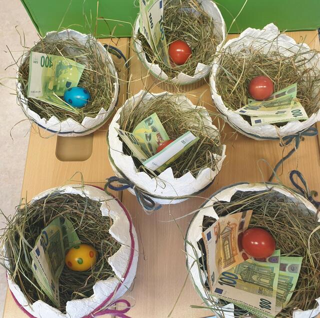 Im Werkunterricht gestaltete Osternester dekoriert mit Heu und „extravielen orangen und grünen Geldscheinen“.