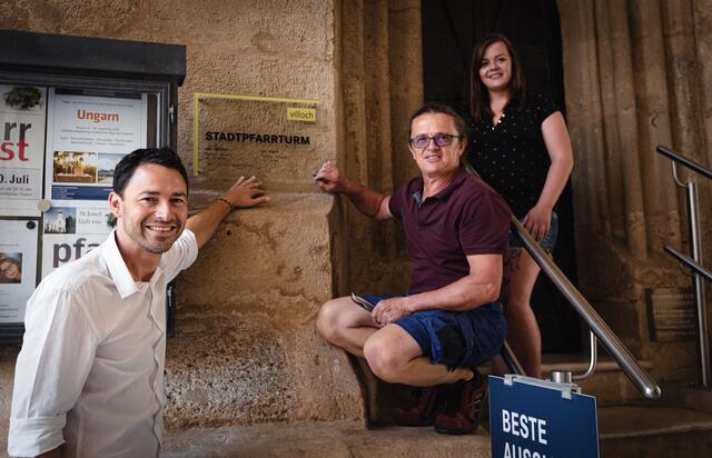 Museumsdirektor Andreas Kuchler, Wirtschaftshof-Mitarbeiter Peter Klotz und „Turmfräulein“ Nicole Krenn bei der Montage des neuen Öffnungszeitenschildes beim Stadtpfarrturm. | Foto:  Stadt Villach/Karin Wernig