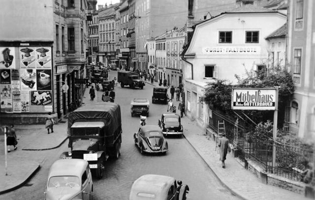 Damals 1952: Straßenszenerie am Graben
Die Aufnahme aus dem Jahr 1952 zeigt den Graben Richtung Landstraße. Bei der Einmündung der Kollegiumgassse auf der rechten Seite finden sich noch drei Häuser, die nach der Schleifung der Stadtmauer in diesem Bereich im letzten Viertel des 18. Jahrhunderts errichtet wurden. Der amerikanische Militärlastwagen im Vordergrund erinnert noch an die Besetzung Österreichs durch die alliierten Truppen bis 1955. | Foto: Archiv der Stadt Linz