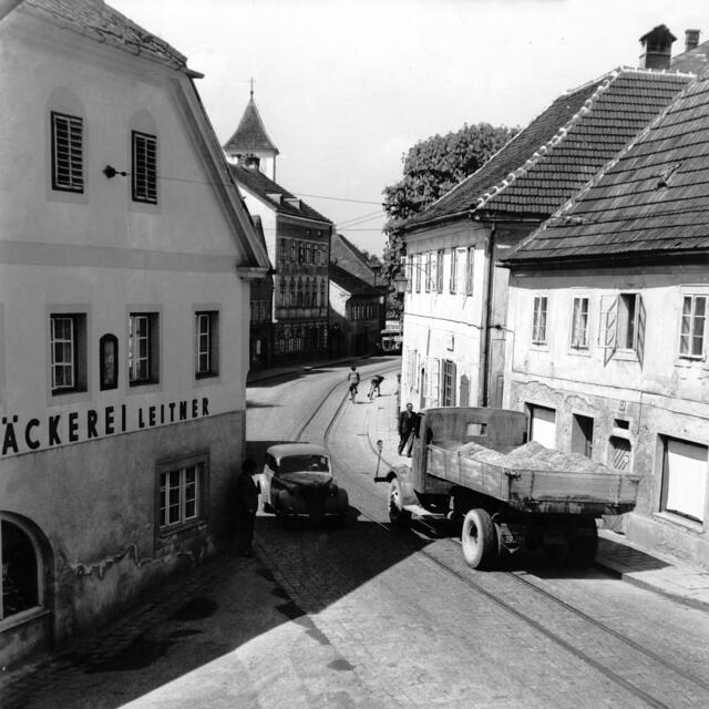 Damals 1952: Das Nadelöhr in Ebelsberg
In den Fünfzigerjahren des 20. Jahrhunderts lässt der Blick von der Einmündung der Kremsmünsterer Straße in die Wiener Straße Richtung Ortszentrum Ebelsberg die prekäre Situation selbst bei noch geringem Verkehrsaufkommen erkennen. Bereits in der Zwischenkriegszeit hatten einige Häuser dem Bedürfnis nach Straßenbegradigung weichen müssen. Die Bäckerei Leitner war das letzte verbliebene Verkehrshindernis. | Foto: Archiv der Stadt Linz