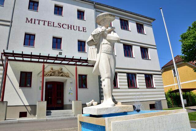 Vogelhändler-Statue des St. Peterer Bildhauers Kunibert Zinner am Vogelhändler-Platz in St. Peter/Au. Im Hintergrund ist das Relief über dem Eingang der Mittelschule, ebenfalls gefertigt von Zinner, zu sehen. | Foto: Hans-Peter Kriener