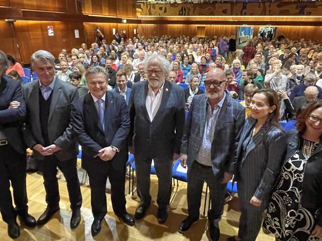 Ein Begrüßungsfoto mit Zeilinger (Mitte) und den Verantwortlichen der VHS und Vertretern der Stadt. Im Hintergrund der voll gefüllte Hörsaal.