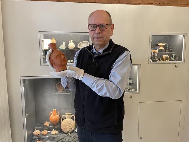 Reinhard Dollinger mit einer römischen Henkelvase in Form eines Mädchenkopfes, die in etwa 300 Jahre n. Chr. entstanden ist.  | Foto: Teischl/RMW