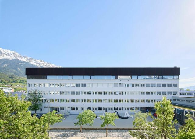 Innsbruck: Die HTL Bau und Design stieß bereits an ihre Kapazitätsgrenzen. Also wurde das Dach des Siebzigerjahre-Schulgebäudes kurzerhand zum Grundstück erklärt und mit einer schwarzen Box aufgestockt. Das Raumerlebnis, sobald man sich durch die Zeitkapsel des alten Stiegenhauses ins fünfte Geschoß hochgearbeitet hat, ist ein luftig leichtes, von Licht und Luft durchflutetes. Über dem umlaufenden Fensterband entfaltet sich ein bis zu sechs Meter hoher Holzleichtbau aus Weißtanne mit einem sinnlichen, weich dahinwogenden Sheddach. Eingespeist wird die Energie über einen neu geschaffenen Fernwärme-Anschluss, der die bisherige Ölheizung ersetzt. Die Lüftungsanlage sorgt für beste Lernluft, dank automatischer nächtlicher Fensterlüftung starten die Maturant:innen auch im Sommer mit kühlem Kopf in den Schultag. | Foto: Lukas Schaller