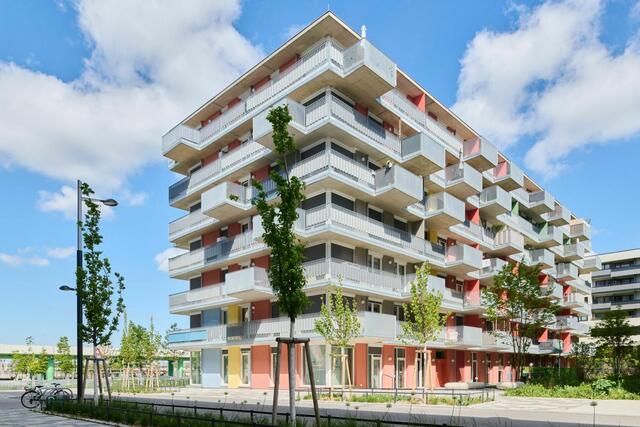 Wien-Seestadt Aspern: Der Gemeindebau Neu in der Seestadt Aspern zeichnet sich durch eine hohe soziale und ökonomische Nachhaltigkeit aus: Hinter der Fassade mit ihren französischen Fenstern, die in Anlehnung an die historischen Bauten des Roten Wien in pastelligen Tönen gestrichen ist, verbirgt sich eine Struktur mit offenen Wohnungsrundrissen und flexibel abtrennbaren Raumzonen zum Arbeiten im Home-Office oder für ein Familienmitglied, das nur am Wochenende zu Besuch kommt. Getrennte elektrische Schaltkreise in den Zimmern ermöglichen es, dass die Mieter:innen die Räume bei Bedarf mit Vorhängen oder Schrankwänden unterteilen und unabhängig voneinander nutzen können. Ein Drittel der insgesamt 74 Wohnungen ist sogar mit raumhohen Schiebewänden ausgestattet. | Foto: Lukas Schaller