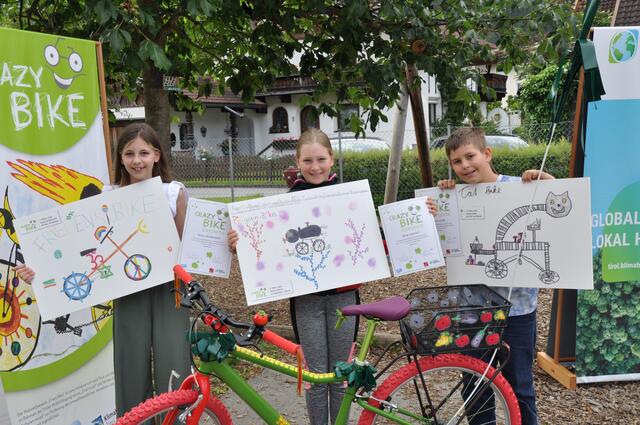 Anna Holzknecht, Nina Lackner und Simon Erdei mit ihren Siegerbildern vor dem Fahrrad der Landessiegerin.