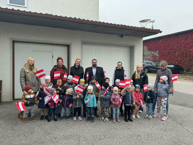 Der Kindergarten Ritzing, Fahnen schwenkend mit dem Bürgermeister. Hier mit: Tobias, Mavie, Florentina, Isabella, Rebecca, Luisa, Lukas, Marie, Ella, Emilia, Tamas, Sarah, Luisa, Humor, Theo, Jonathan, Mark, Raphael, Emily, Lea, Lena Martna, Sylvia Trettner, Kindergartenleiterin Julia Martna, Bürgermeister Jochen Müllner, Praktikantin Zsofia, Praktikantin Maya und Andrea Hahn.
 | Foto: Gemeinde Ritzing