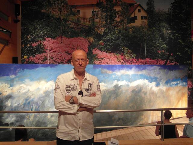 Herbert Brandl vor seiner kombinierten Arbeit mit Garten und Heimathaus quasi als Fatamorgana mit vorgelagertem modernem Sujet in monumentalem Querformat. | Foto: Susanne Veronik