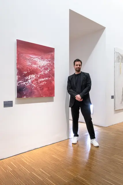 Der Künstler Hans Peter Perner neben seinem Gemälde „Übergang in die Unendlichkeit“ (2024, Öl auf Leinwand), ein leuchtend rotes, abstrahiertes Gletschermotiv.  | Foto: Roberto Grill Galerie Grill