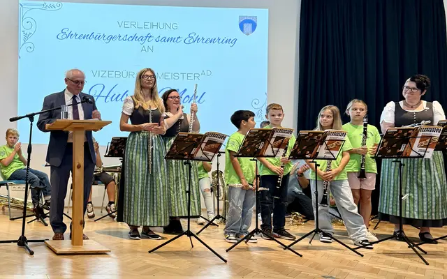 Alt-Vizebürgermeister und Ehrenbürger Hubert Mohl bei seiner Dankesrede; re. Musikverein Wöllersdorf-Steinabrückl mit Kindern aus dem Jugendblasorchester