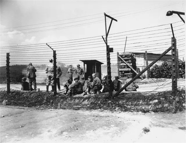 Befreite Häftlinge an einem offenen Zaunstück mit einem US-Soldaten im Hintergrund. Mauthausen, Mai 1945. | Foto: USHMM (United States Holocaust Memorial Museum), courtesy of Eugene S. Cohen