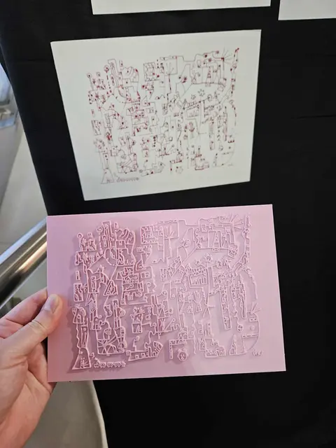Kunstwerk von Viktoria Vöros

Das BIld zeigt eine abstrakte Zeichnung mit vielen kleinen Details in roter Tinte auf weißem Papier. Das BIld hängt auf einem schwarzen Untergrund. Im Vordergrund sieht man eine 3D gedruckte Platte in rosa Farbe, auf der das gleiche Bild durch erhabene Linien ertastbar ist.