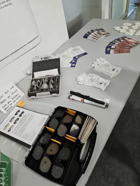 Tisch mit Gegenständen zum Ausprobieren

Ein grauer Tisch, auf dem unterschiedliche Gegenstände liegen: Brillen, die verschiedene Sehbeeinträchtigungen visualisieren, ein Blindenstock, Lormen-Handschuhe, Informationen dazu