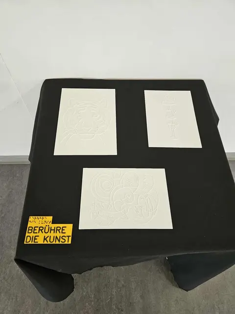 Modelle von Kunstwerken der taubblinden Künstlerin Lydia Kremslehner

Ein quadratischer Tisch mit schwarzem Tischtuch. Darauf liegt eine gelbe 3D gedruckte Platte, auf der in schwarzer Schrift und Braille steht "Berühre die Kunst". Daneben liegen drei 3D gedruckte Platten, auf denen Kunstwerke durch erhabene Linien ertastbar gemacht werden.