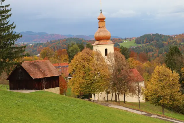 Ein Ausflug nach Sankt Bartholomä ist zu jeder Jahreszeit schön, besonders aber im Herbst. Heuer wurde der Zwiebelturm auf der historischen Alten Kirche renoviert und mit Holzschindeln gedeckt. Im September erfolgte die Eröffnung des Hanns-Koren-Museums in der Alten Kirche. Ein nur 13 m2 kleiner Raum lässt in das Wirken des früheren LT-Präsidenten und verdienstvollen Steirers blicken. Neben Korens (1906-1985)  markanten Hut und Wetterfleck gibt ein digitales Buch Auskunft über das Leben des Volkskundlers, der mit Tradition und Brauchtum eng verbunden, aber als Kulturpolitiker auch den modernen Strömungen aufgeschlossen war. Er prägte den Satz "Heimat ist Tiefe, nicht Enge″ und wählte Sankt Bartholomä zu seiner Wahlheimat. Das Foto zeigt den Platz der Alten Kirche in seiner Herbstschönheit am 26. Oktober 2025. 
 | Foto: Edith Ertl