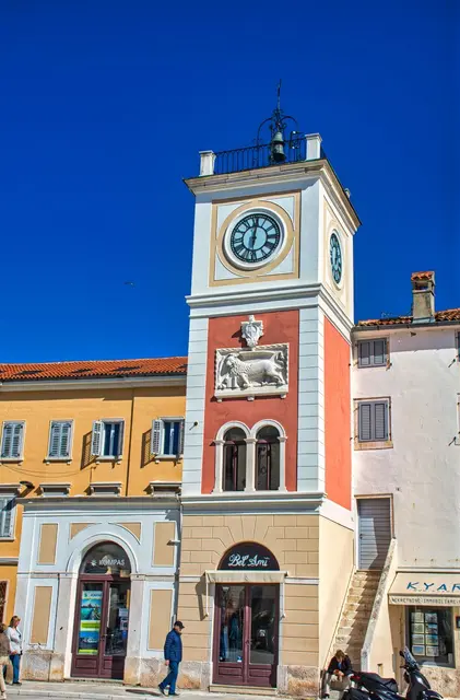  Sie befindet sich auf dem Hauptmakrtplatz in Rovinj. Einmal war sie der Südturm der Stadtmauern. Dieser Turm wurde mehrmals in der Geschichte nachgebaut, jedoch dadiert sein Aufbau auf den 12. Jh. Unter dem Turm befand sich einmal das Gefängnis für kleinere Reliktaten. Die Stadtuhr aus der Mitte des 19. Jhs. mit dem venezianischen Löwen, dem Symbol der Serenissima (Republik Venedigs), befand sich auf dem Turm der Stadttore in der Nähe des Palastes Califfi. aus rovijn turismus.com