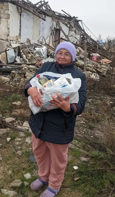 Frau mit Lebensmittelspenden vor ihrem zerstörten Haus in der Ukraine. | Foto: SSTA