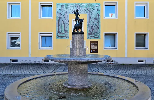 Jupiter-Dolichenus-Brunnen des Bildhauers Albrecht Fürthner im Zentrum von Mauer, Stadtgemeinde Amstetten. Im Hintergrund an der Fassade des Mehrparteienwohnhauses Hauptstraße 15: Abdruck des Sgraffitos (Original hinter dem Vollwärmeschutz) von Willy Hengl aus dem Jahr 1955. | Foto: Hans-Peter Kriener