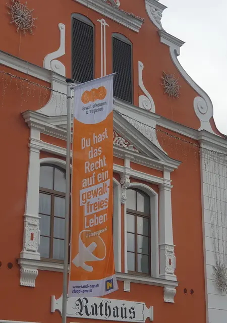 Gemeinde Bildinfo: Mit einer Fahne vor dem Rathaus und der in orange beleuchteten Stadtmauer macht Groß-Enzersdorf auf das Recht von Frauen und Mädchen auf ein gewaltfreies Leben aufmerksam. | Foto: Gemeinde Groß Enzersdorf