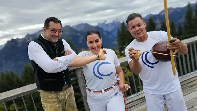 Foto: Die Capoeirista Christina Tschofen (mi) und ihr Mestre Hayu (re) zeigen Andreas Seeburger (li) nach der Muttersberg-Fernsehgondelfahrt, auf der Alpengasthof-Panoramaterrasse ihre Sportart in Aktion.