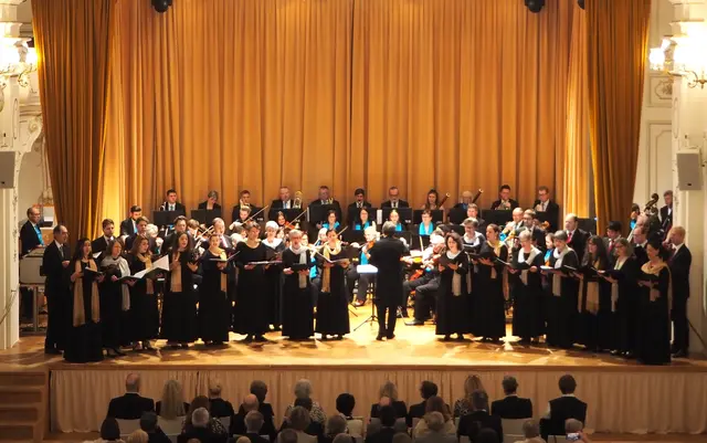 Konzertaufstellung vor der Pause mit dem Damenvokalensemble Indigo &amp; Herrenvokalensemble Cantores. und dahinter dem Sinfonischen Orchester MERKUR.