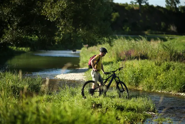 Ein Radfahrer genießt die frische Luft und die idyllische Landschaft entlang der Mittelpunkt-Radroute. Das sanfte Plätschern des Wassers und das sanfte Rascheln der Gräser schaffen eine entspannende Atmosphäre, die zum Verweilen einlädt. | Foto:  Mostviertel Tourismus/weinfranz.at
