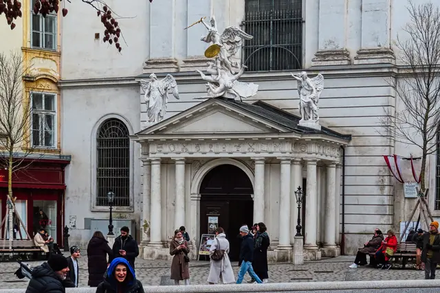 Gleich gegenüber prunkt der Eingang in die Michaeler-Kirche mit seiner Portalkrönung, dem gefallenen Engel