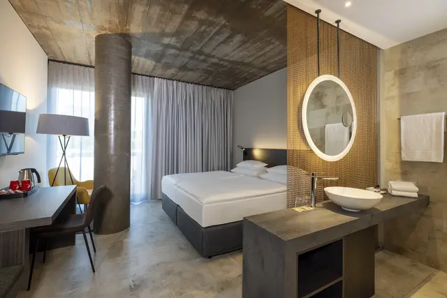  Die 189 Zimmer und Suiten interpretieren das industrielle Erbe der Tabakfabrik neu: Sichtbeton, Metallakzente und klare Linien treffen auf hochwertige Materialien und zeitgemäßen Komfort. 