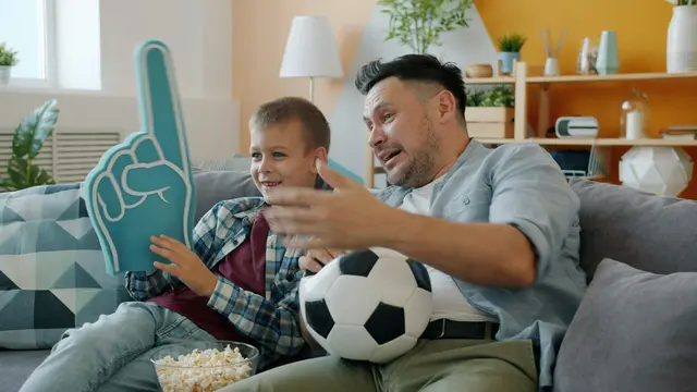 Vater sitzt mit Sohn auf der Couch und wartet auf das Fußballmatch.